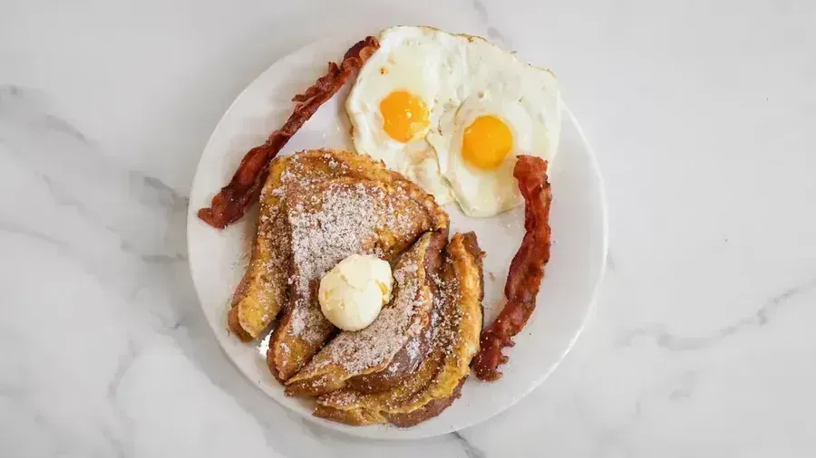 French toast with butter beside bacon and fried eggs on a marble table at Harry's Cafe, Katella Ave, Stanton, CA