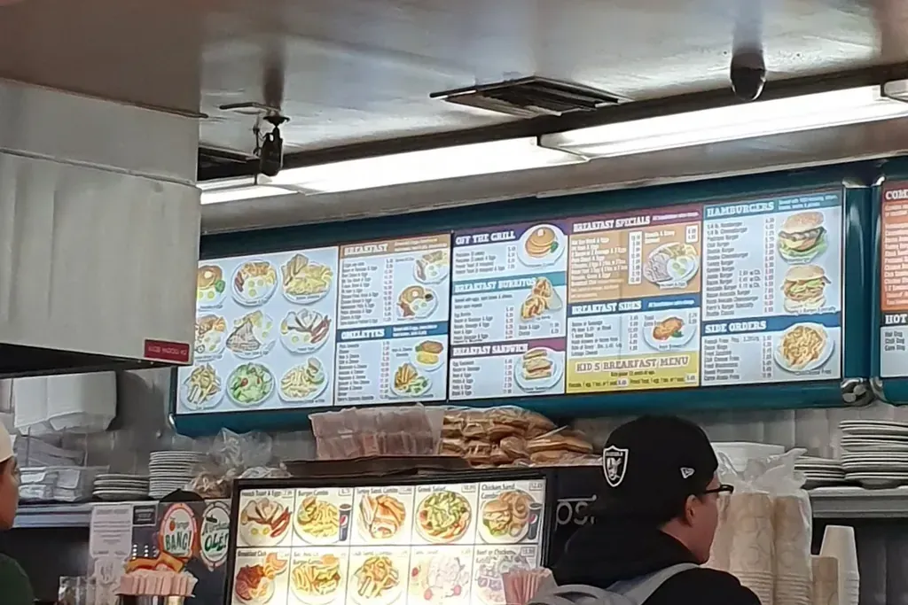A guest ordering at the counter under the menu screens at Harry's Cafe, Katella Ave, Stanton, CA