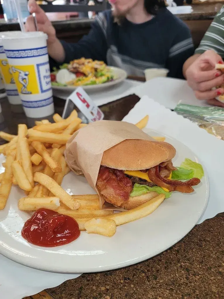 A bacon cheeseburger wrapped in paper with french fries at Harry's Cafe, Katella Ave, Stanton, CA