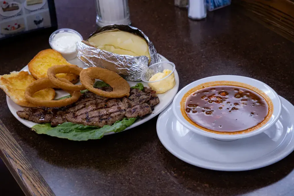 A grilled steak plate with onion rings, a baked potato, garlic toast and a bowl of soup at Harry's Cafe, Katella Ave, Stanton, CA