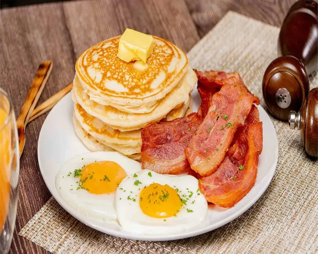 A stack of pancakes with butter, bacon and two fried eggs at Harry's Cafe, Katella Ave, Stanton, CA
