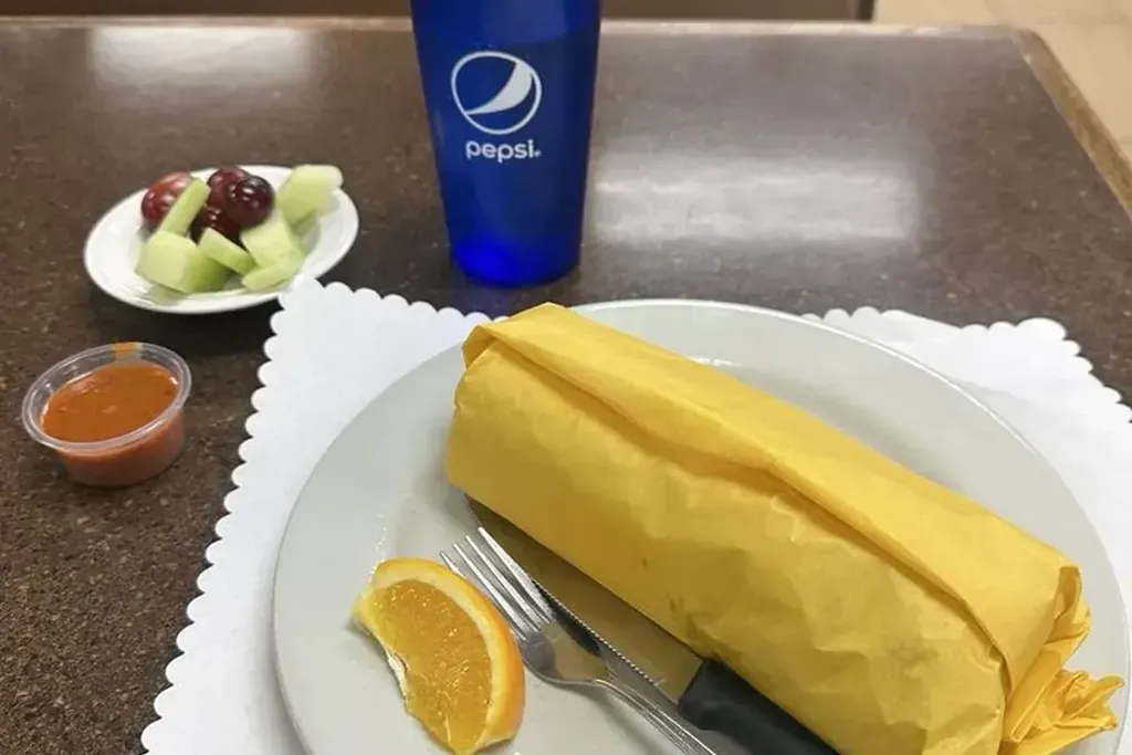 A breakfast burrito wrapped in yellow paper with salsa and an orange slice at Harry’s Cafe, Katella Ave, Stanton, CA.